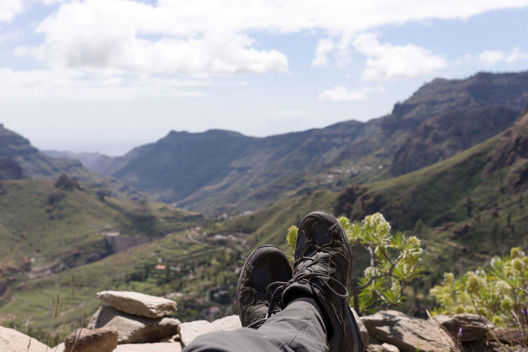 Low section of person relaxing on mountain against sky