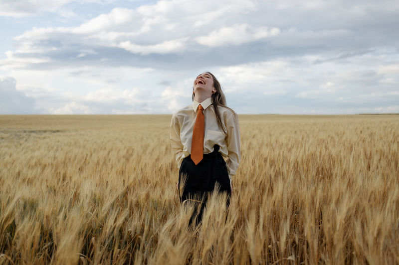 Side view of woman standing amidst wheat field against sky