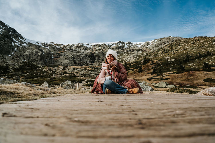 Full length of man sitting on rock against mountain