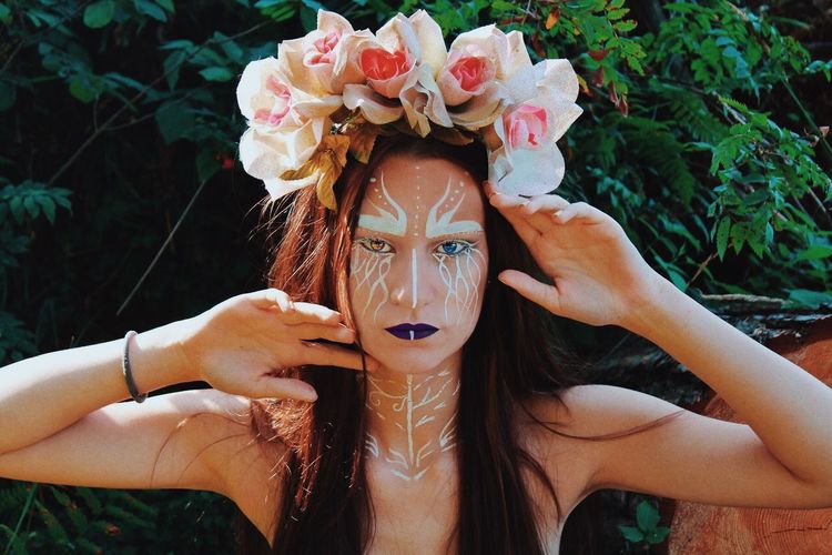 Portrait of shirtless young female model with face paint against plants