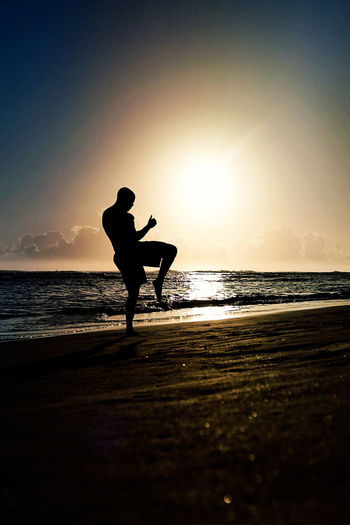 Silhouette athlete practicing kickboxing at beach against clear sky during sunset