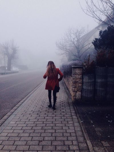 Rear view of woman walking on sidewalk in foggy weather