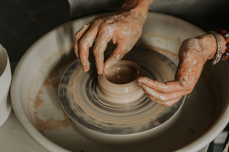 Close-up shot of ceramic cup spinning on potters's wheel and hands molding clay