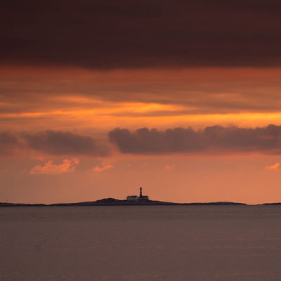 Silhouette of lighthouse on sea during sunset