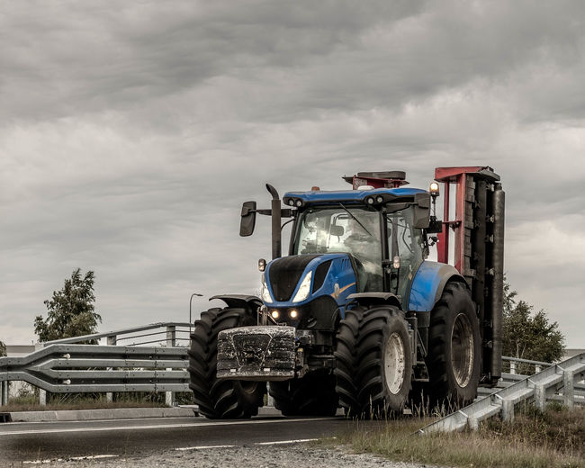 Tractor on road amidst field against sky