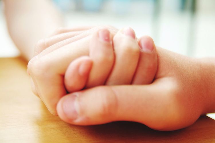 Close-up of parent and child holding hands on table