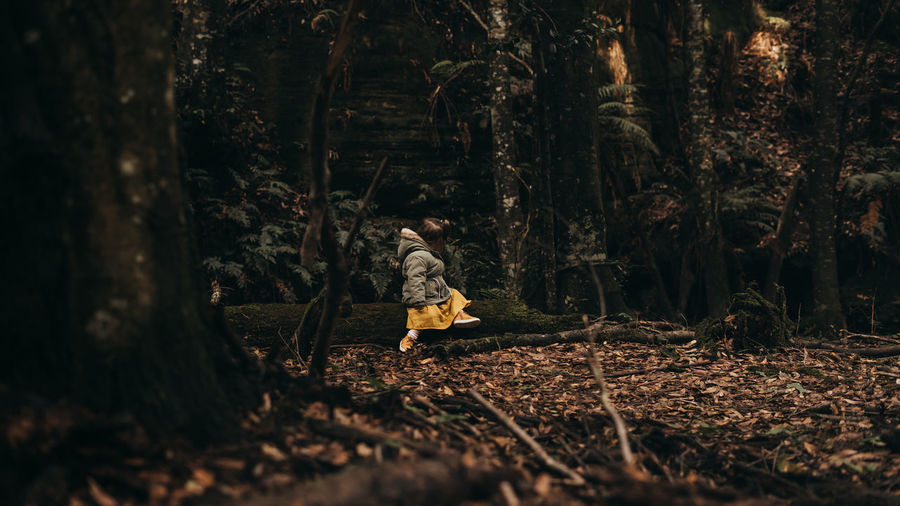 Cute girl sitting by trees in forest