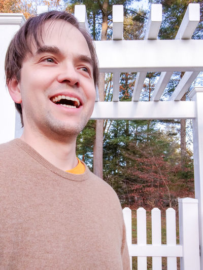 Portrait of smiling man standing by fence against trees