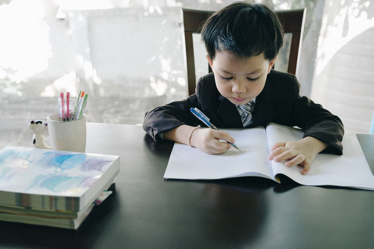 Boy writing in book on table
