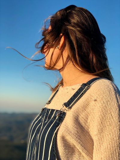 Woman with tousled hair against blue sky at sunset