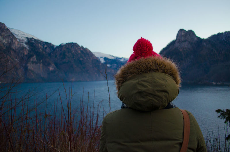 Rear view of woman in warm clothing looking at river and mountains