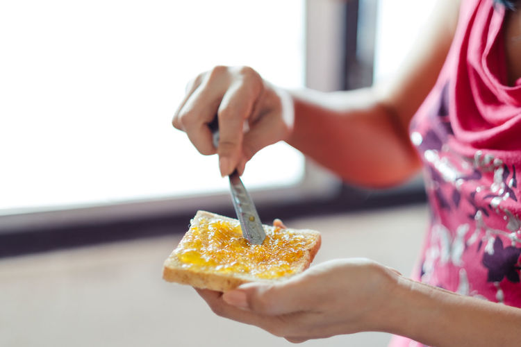 Midsection of woman spreading orange jam on bread at home