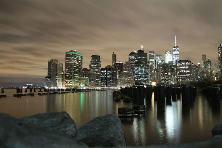 Illuminated city by river against sky at night