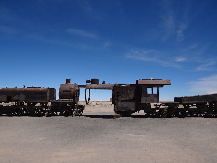 Abandoned train on field against blue sky