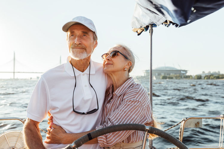 Low angel view of couple standing on sailboat against sea
