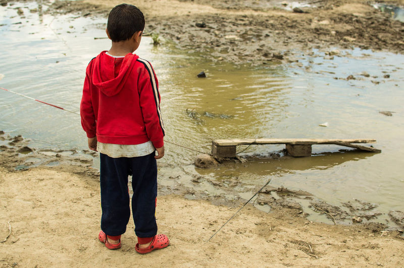 Rear view of boy standing by puddle at refugee camp