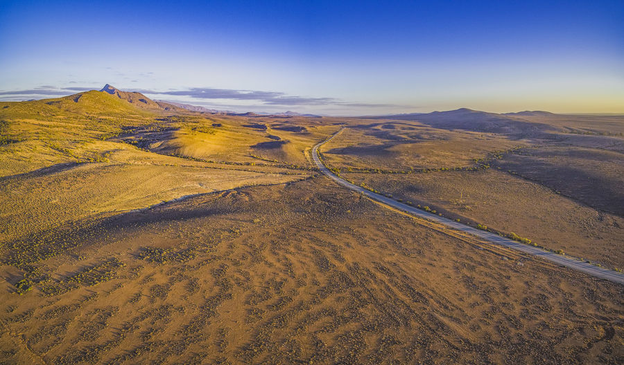 Rural road passing through dry land with scarce peaks at sunset - aerial panorama aerial shot