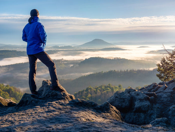 Hiking in sunrise. man hiker wear hood and blue windcheater stay alone in sunset at mountain edge