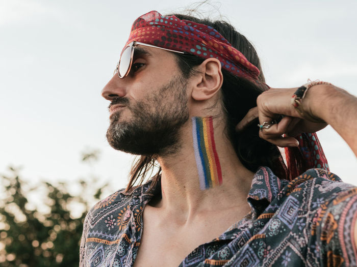 Side view of a emotionless man with lgtbi flag painted on his neck.