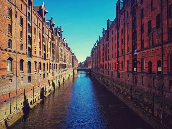 Canal amidst buildings against blue sky