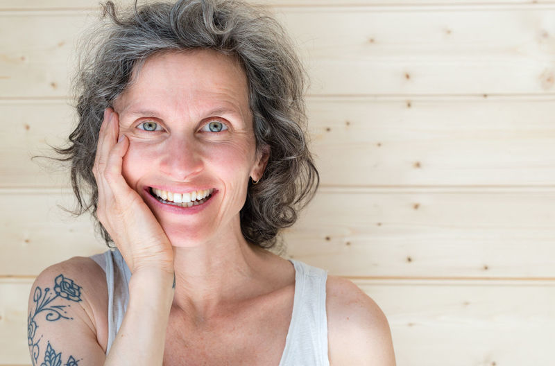 Close-up portrait of happy mature woman with hand on chin by wall