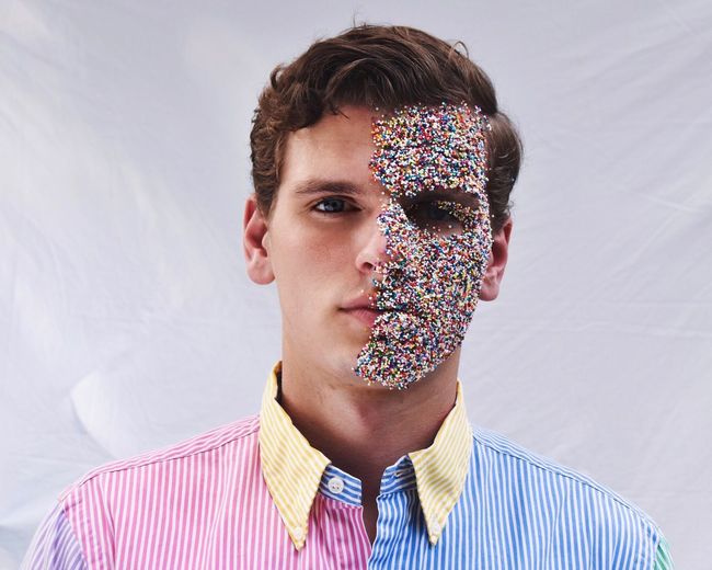 Portrait of young man with colorful sprinkles on face by white wall