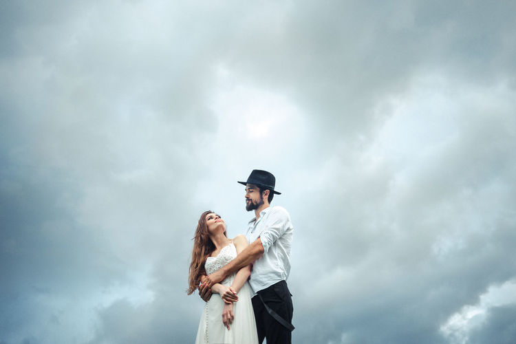 Low angle view of man embracing woman while standing against cloudy sky