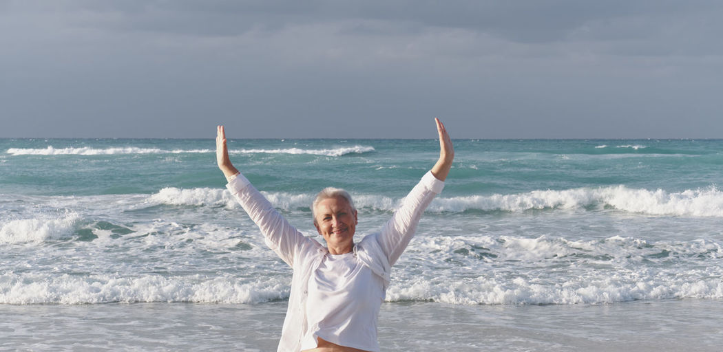 Happy smiling caucasian senior woman with outstretched arms over background of atlantic ocean, cuba.