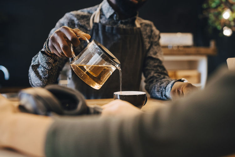 Midsection of male owner pouring tea in cup at coffee shop