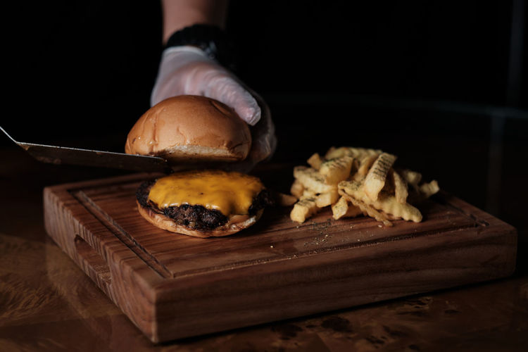 Cropped hand of chef cutting hamburger