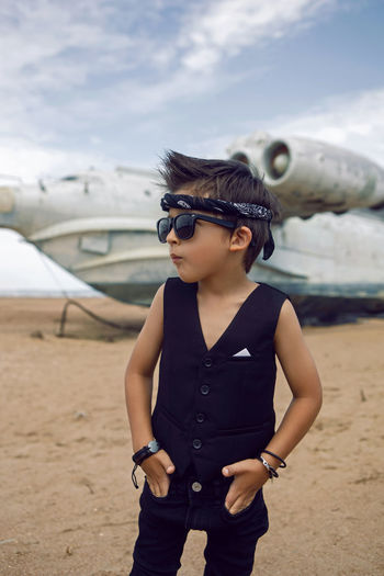 Rocker boy a child in black clothes stands against the plane on the beach in summer in dagestan