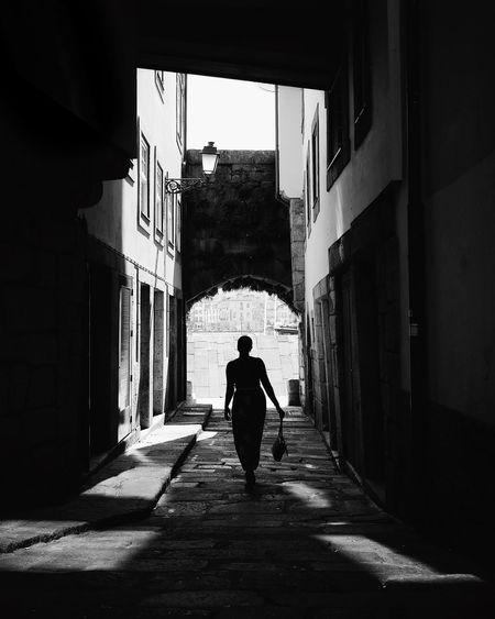 Rear view of woman walking at alley amidst buildings in city