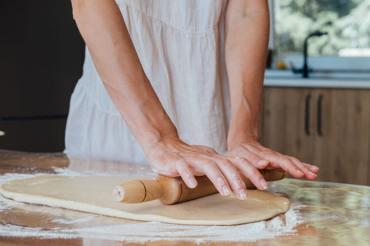 Close up of young woman rolling dough with rolling pin for homemade bakery.