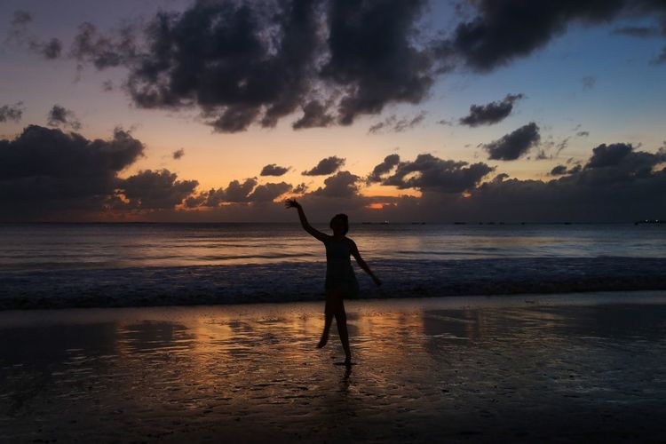 Silhouette woman dancing at beach against sky during sunset