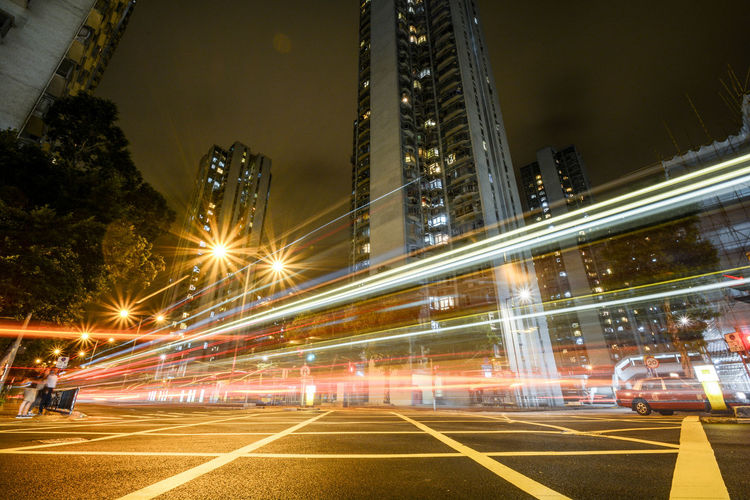 Light trails on city street by buildings against sky at night in hong kong 