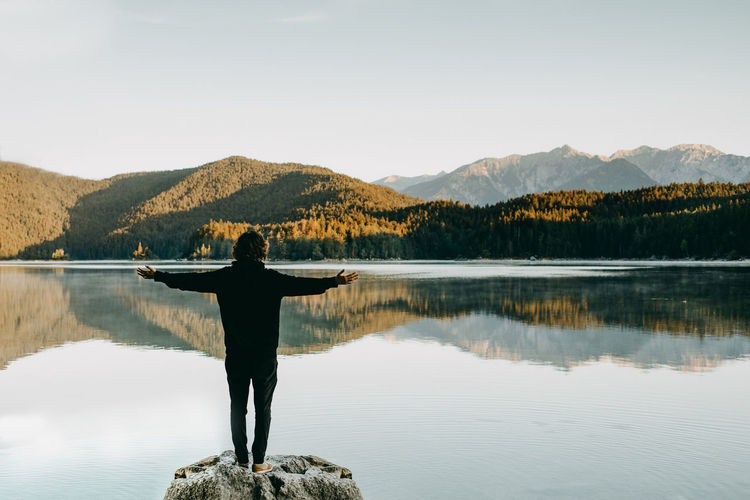 Rear view of man standing by lake against sky
