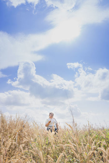 Man sitting on grass in field against sky