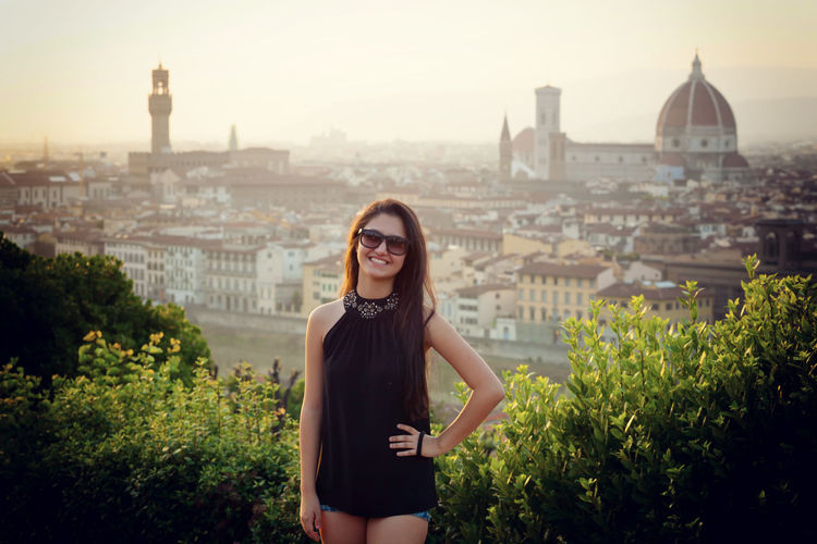 Portrait of smiling young woman standing against cityscape 