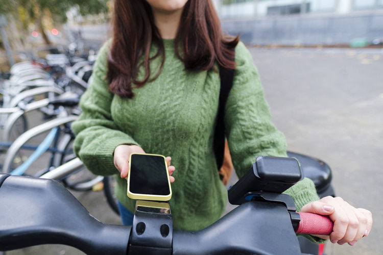 Hand of woman renting electric bicycle through smart phone at station