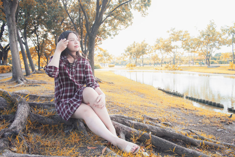 Young woman sitting on tree against plants