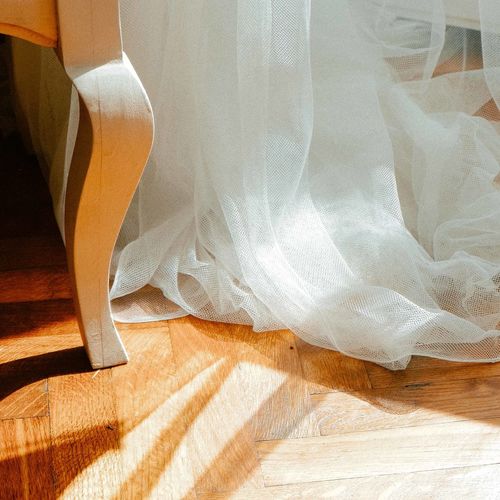 Detail of a chair leg and a white curtain on hardwood floor