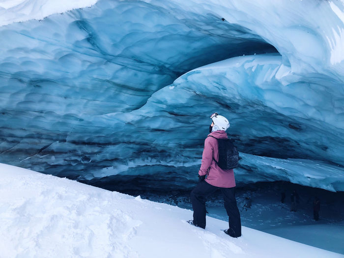 Woman standing next to blue ice cave