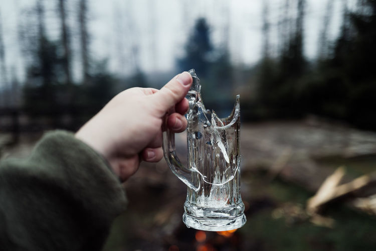Close-up of person hand holding glass against trees during winter