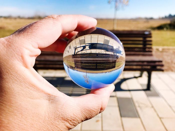 Cropped hand holding crystal ball with reflection of bench