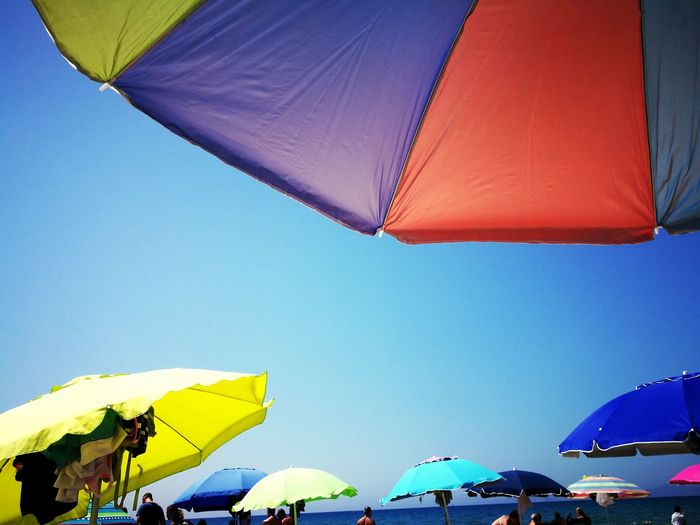 Colorful parasols and people at beach against clear blue sky