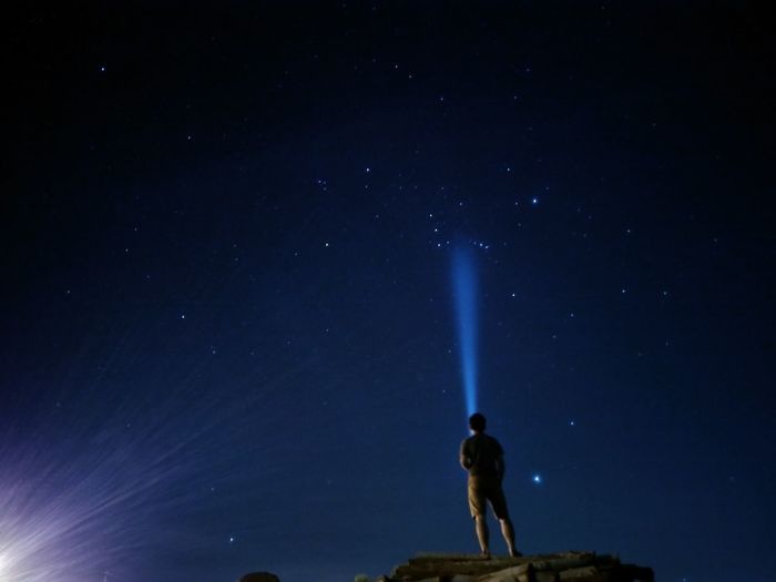 Man with flashlight standing against sky at night