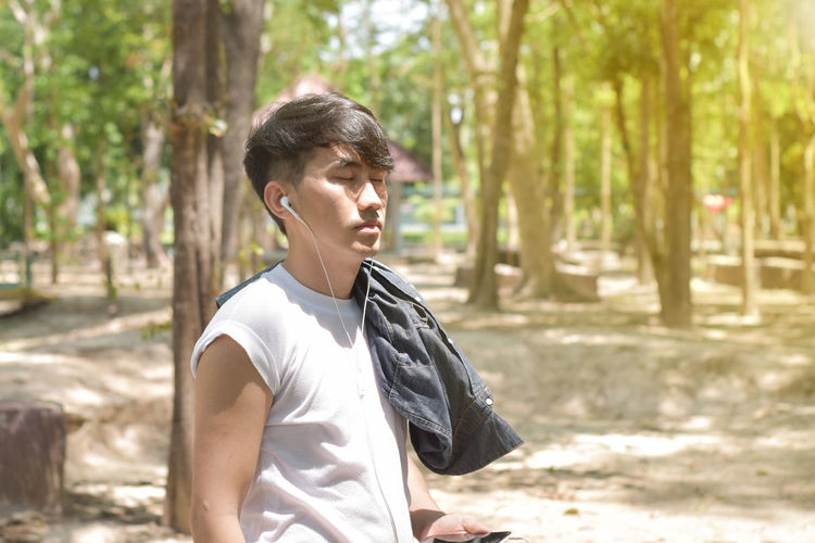 Man wearing white headphones and listening to music on his smart phone standing in the park.