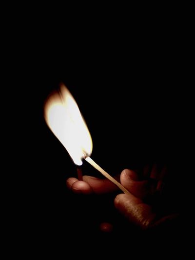 Close-up of hand holding burning matches against black background