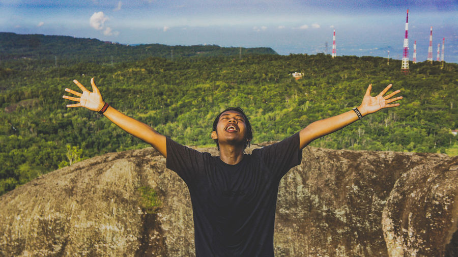 Man with arms outstretched standing on mountain against sky
