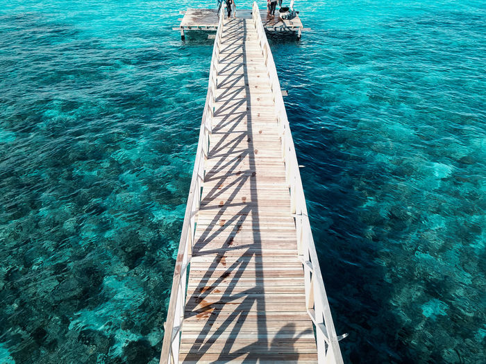 Aerial top view of wooden pier bridge, walkway to the sea in cleared and clean seawater
